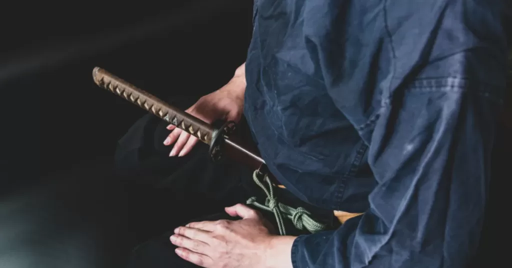 Samuraj z kataną u pasa siedzi na kolanach w dojo i medytuje nad oddechem